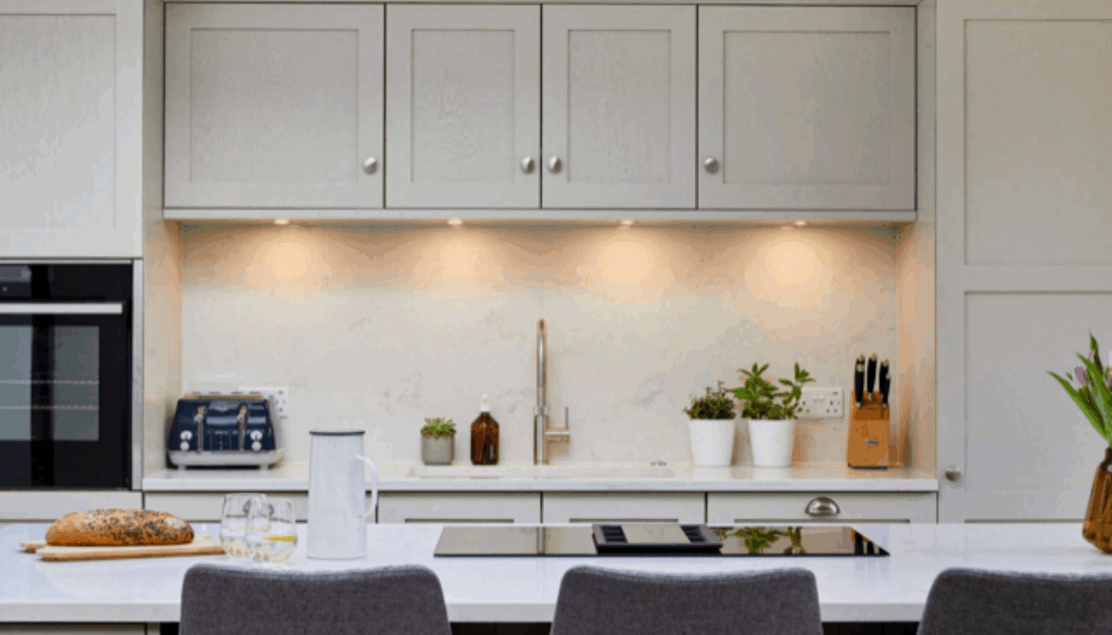 Modern kitchen with LED under cabinet puck lights illuminating white countertops and cabinets, showcasing a bright and energy efficient lighting upgrade